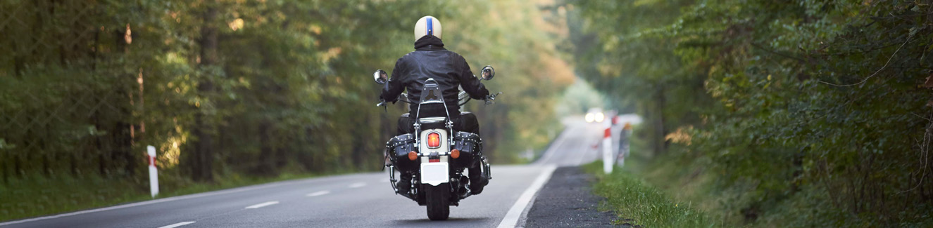 Biker in black leather outfit driving modern powerful motorcycle along sunny road on summer day